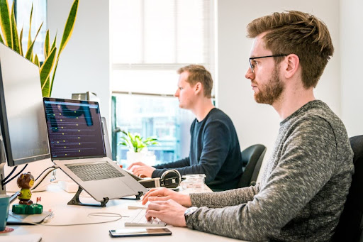 Two men in an office setting, working on laptops and using professional services automation software